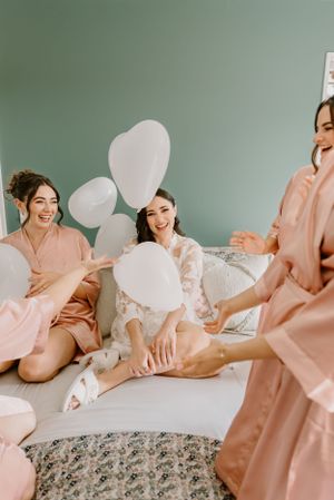 Friends in pink robes celebrate on a couch with white balloons at a bridal party gathering.Trents Vineyard, Christchurch photographer