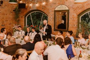 A wedding reception dinner party in a rustic brick venue with string lights overhead and guests seated at long tables.