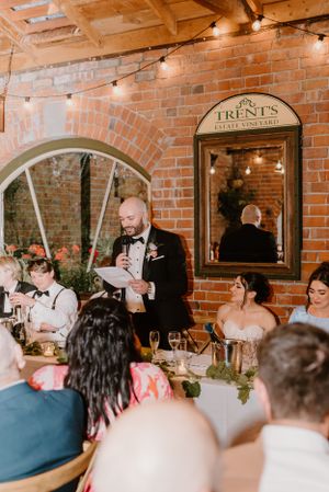A wedding reception in a rustic brick venue with string lights and guests gathered for dinner and toasts.