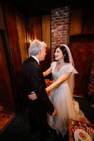 Bride in white gown and veil shares a joyful moment with older man in tuxedo at elegant wedding venue.