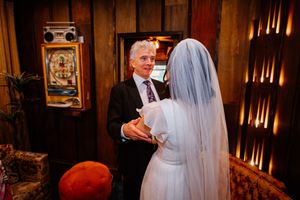 Bride in white gown and veil shares a tender moment with groom in tuxedo at a warmly lit wedding venue.