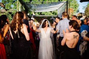 Bride in white gown and veil walks through cheering wedding guests outdoors at a garden reception celebration.