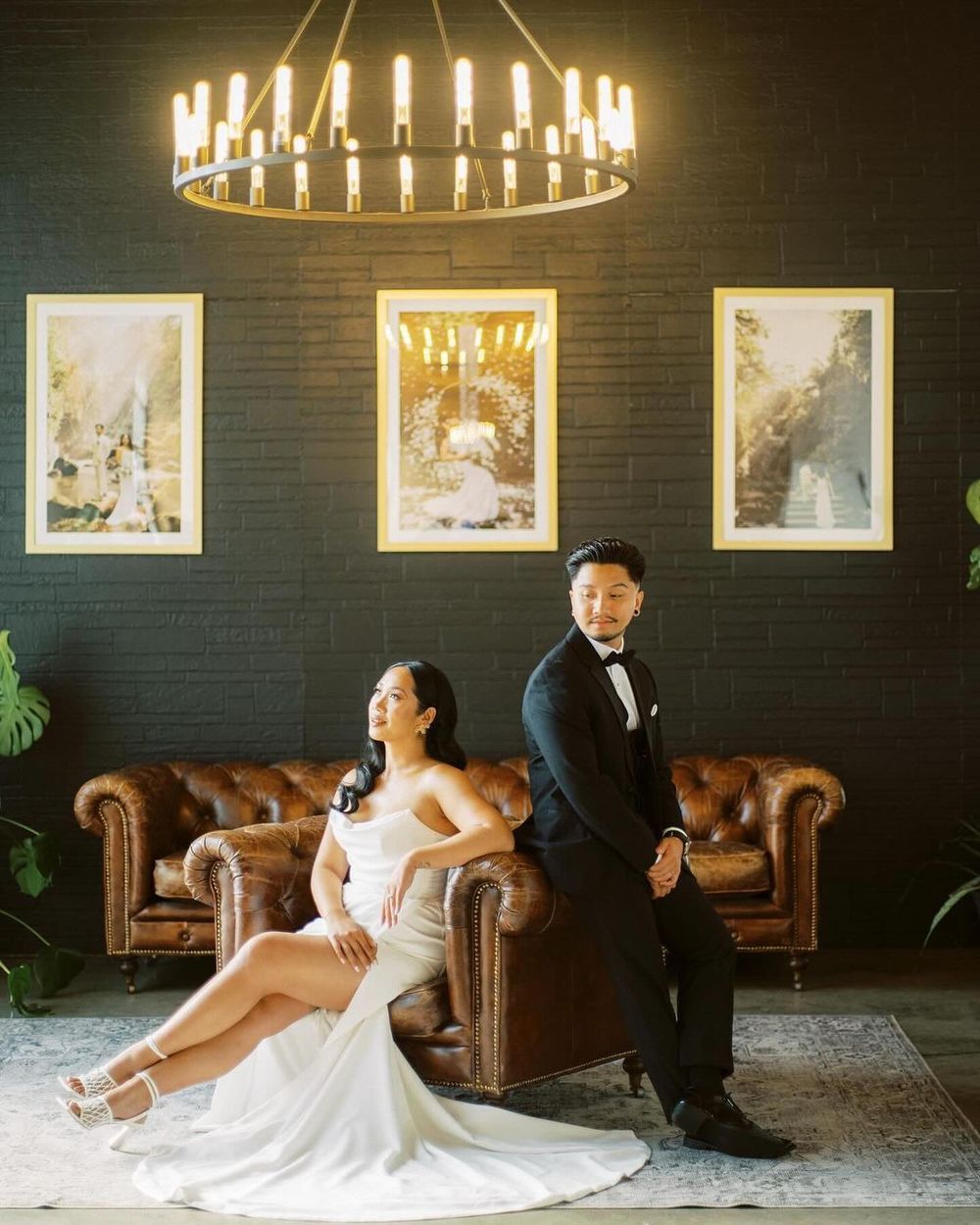 Elegant wedding portraits in dark room with chandelier and leather couches creating moody ambiance.