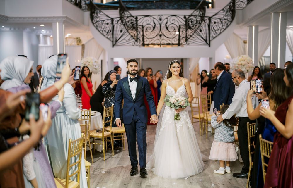 A wedding celebration in an elegant venue with guests lining the aisle as a couple walks down the aisle together.