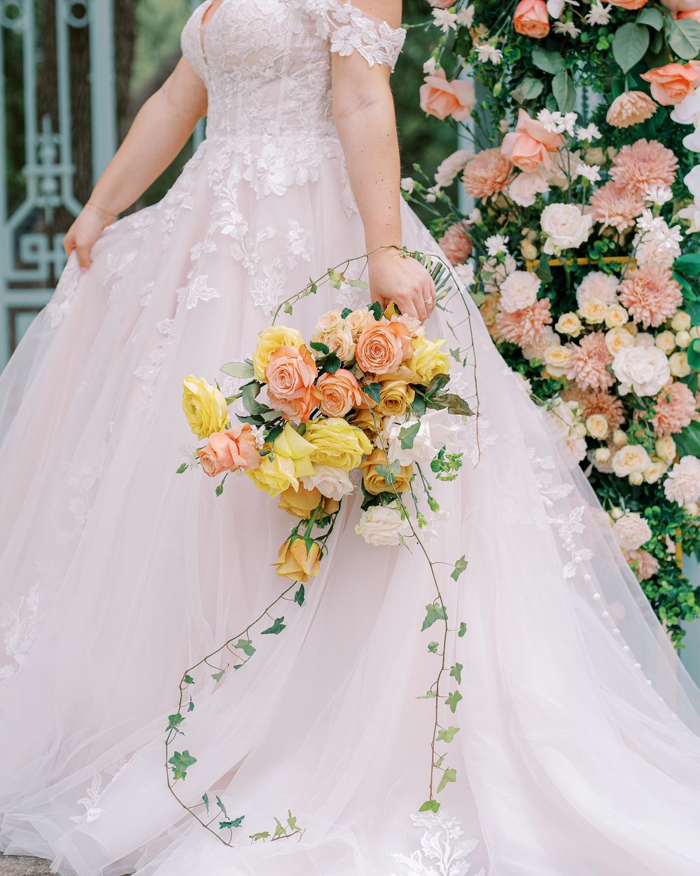 Close-up details of a blush pink wedding dress with coral and yellow floral bouquet arrangements.