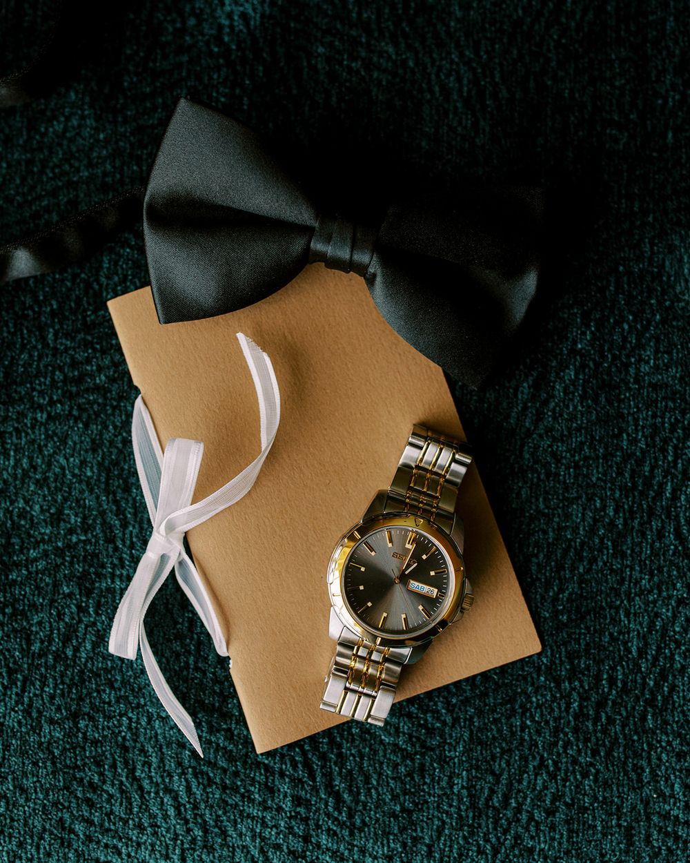 Gold watch and white ribbon styled on dark textured surface in minimalist wedding detail shot.
