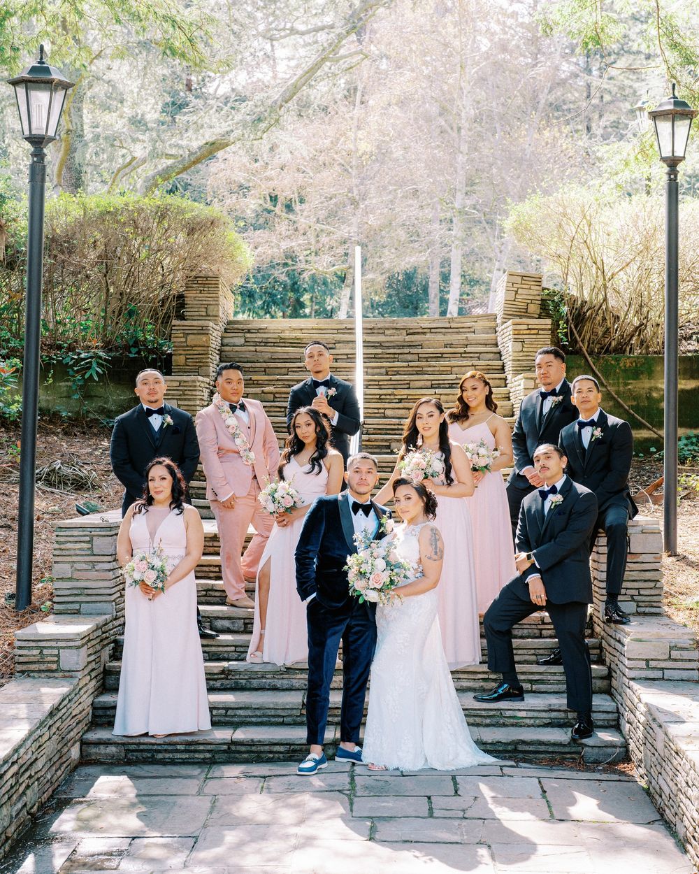 Wedding party poses on outdoor stone steps with bridesmaids in pink dresses and groomsmen in dark suits.