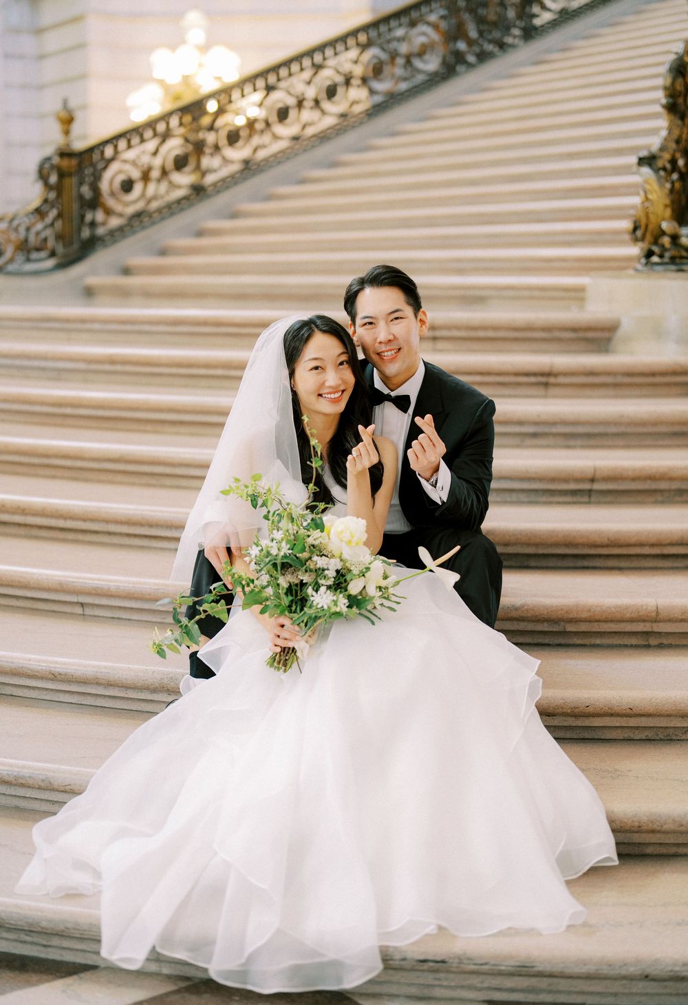 Wedding couple poses playfully on grand stone steps with white dress flowing in romantic outdoor photoshoot.