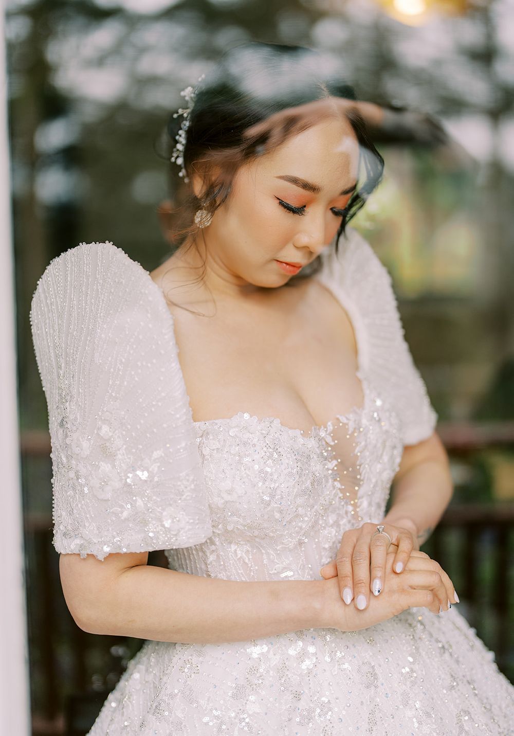 A bride in an elegant white lace wedding dress with puffy sleeves poses gracefully in a romantic outdoor setting.
