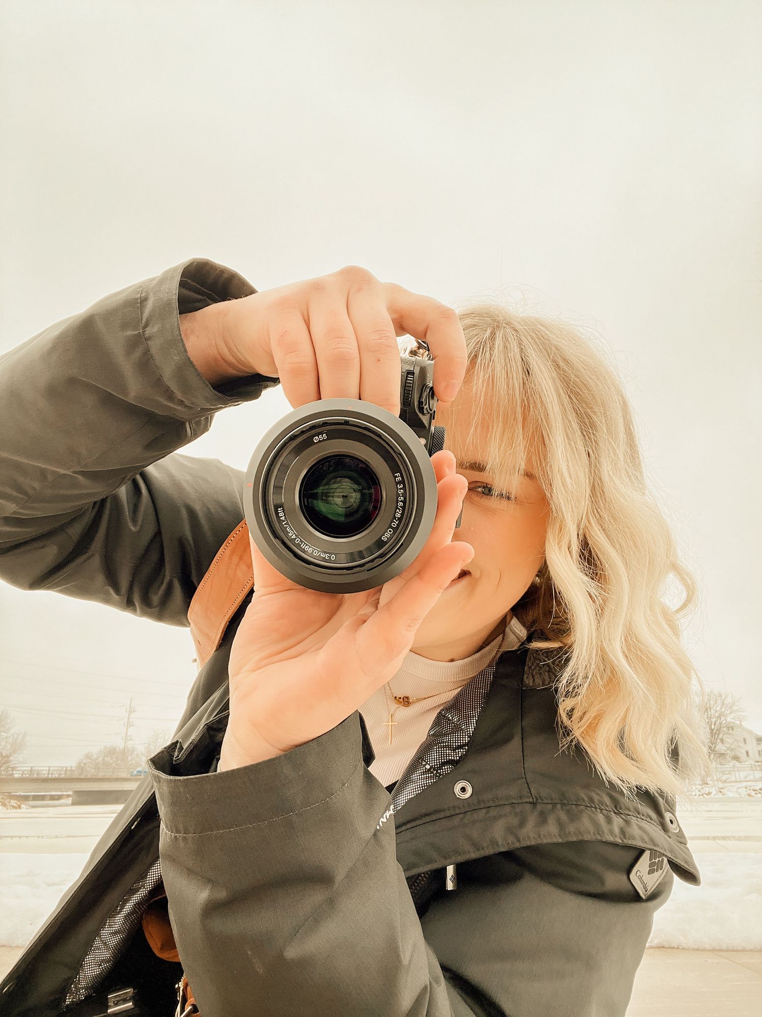 Person holding a camera with lens against neutral background.