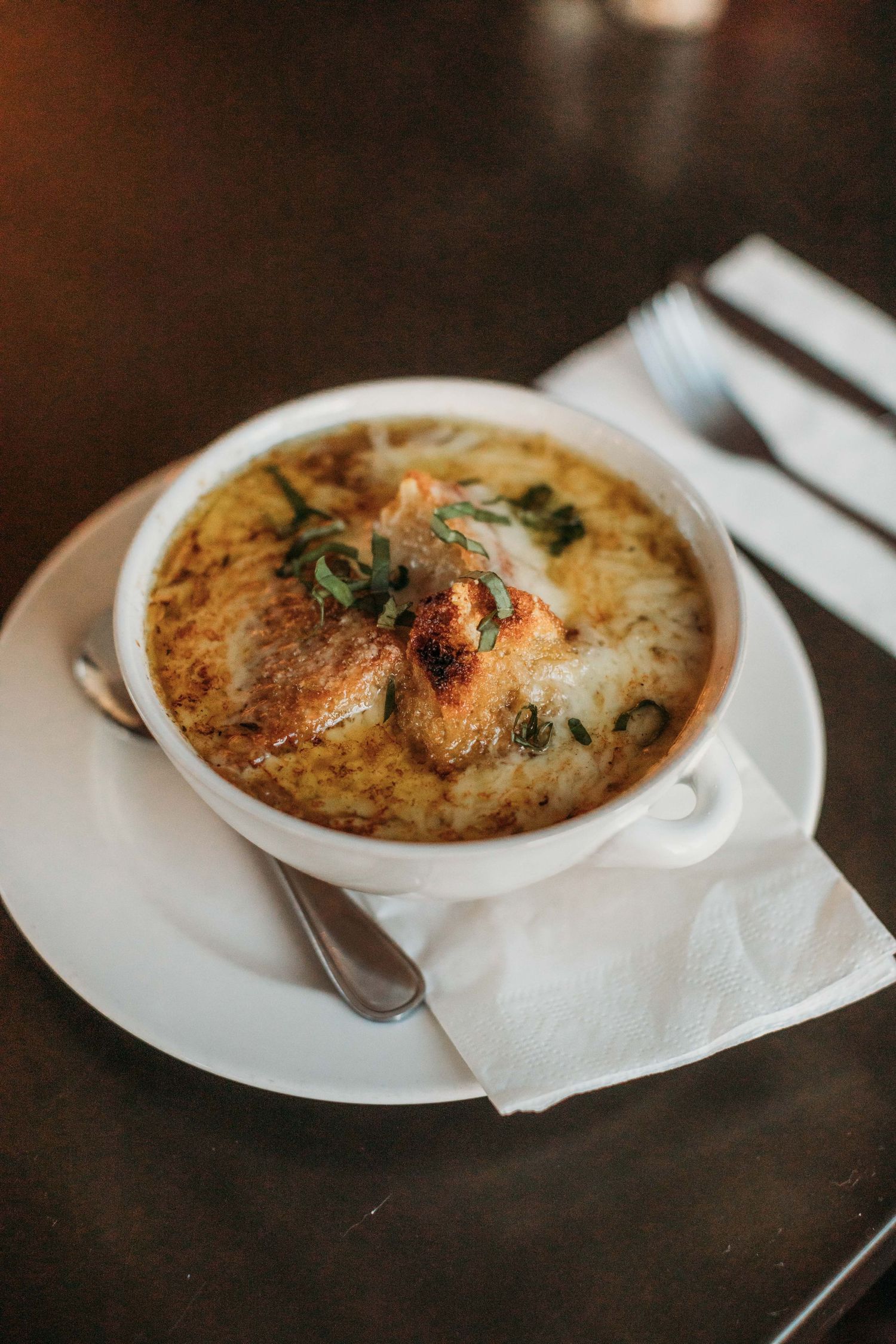 French onion soup in white bowl, on white bowl.