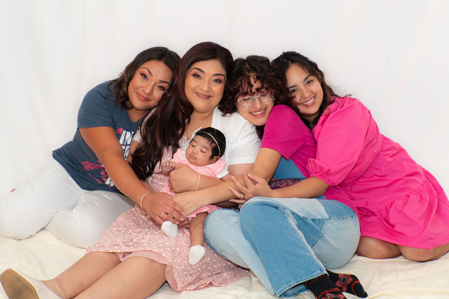 Four women and a newborn baby pose together for a sweet family portrait indoors.