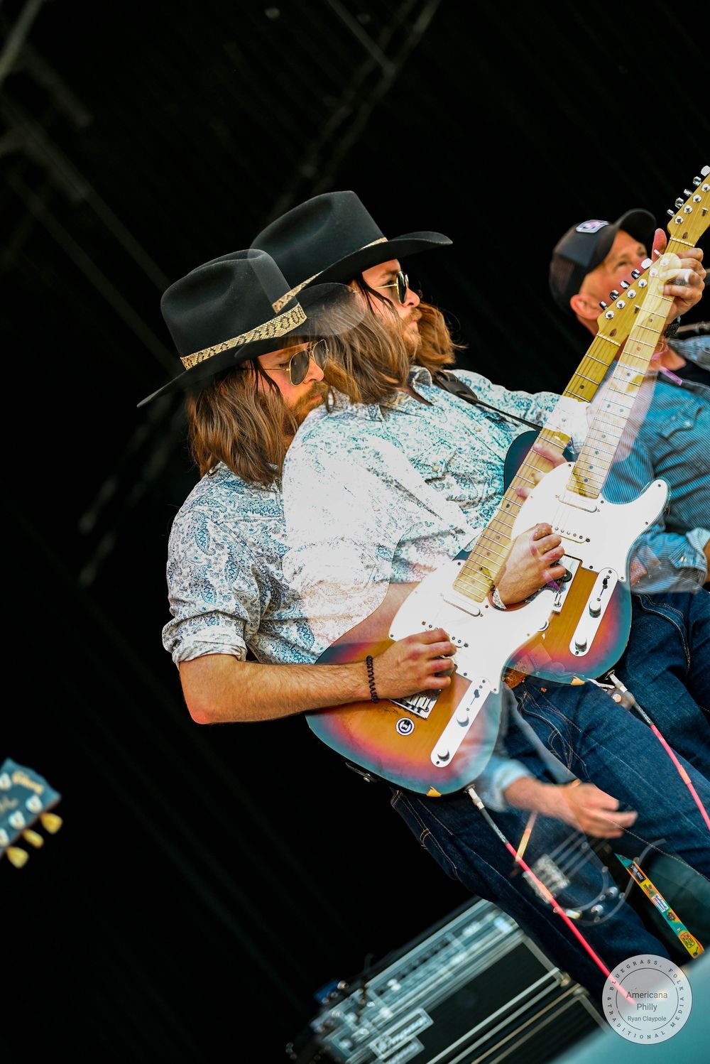 Two musicians in cowboy hats playing electric guitars on stage at an outdoor concert.