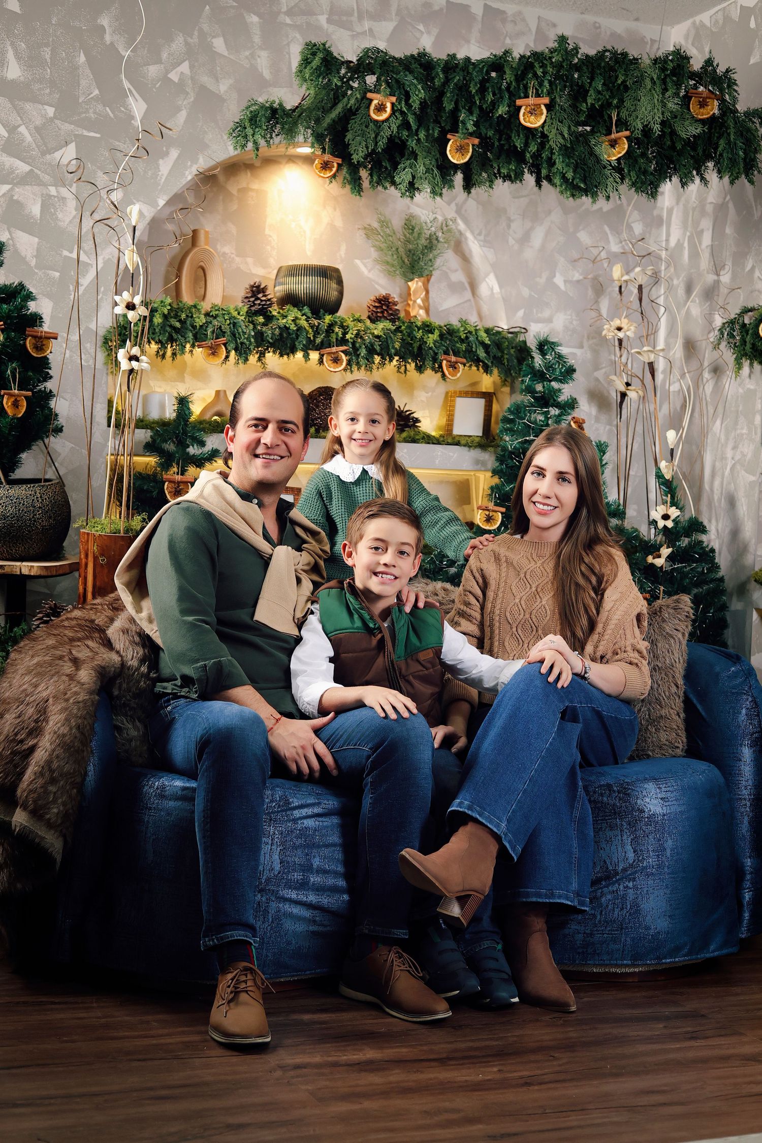 Cozy Christmas living room with blue sofa, evergreen trees, candles, and rustic shelves decorated with holiday ornaments.