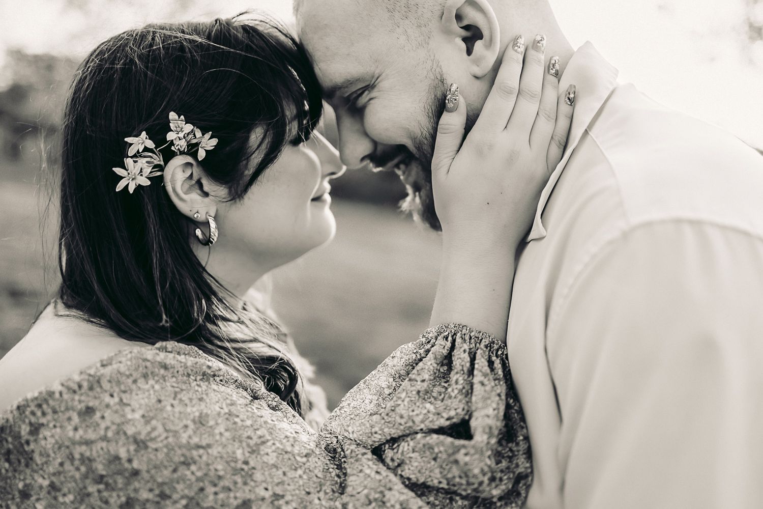 Black and white photo of a romantic couple touching foreheads, bride with flowers in hair, sharing an intimate moment.