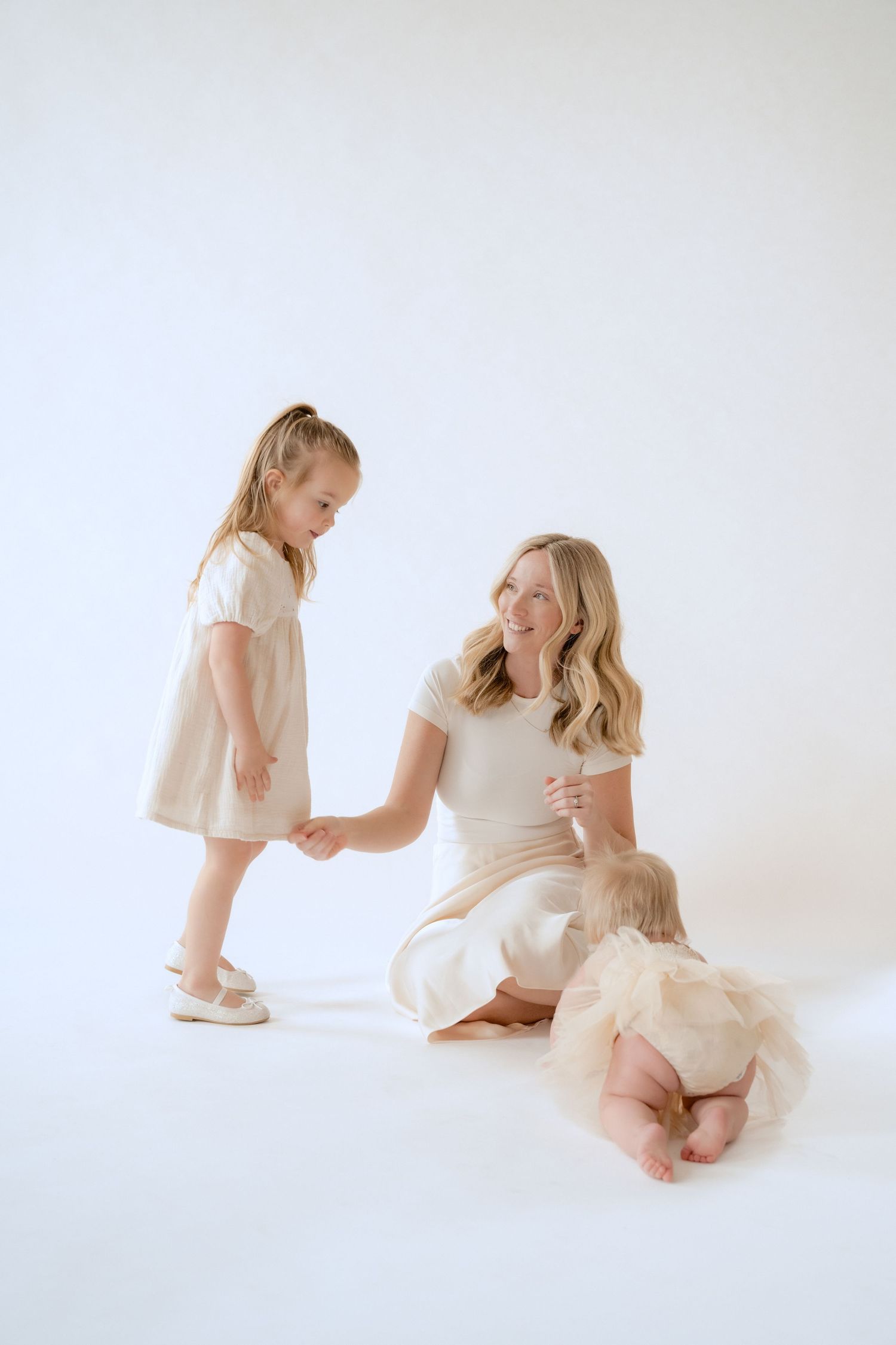 Mom smiles at toddler while baby crawls across the studio floor during an in-studio family session in Stillwater, MN.