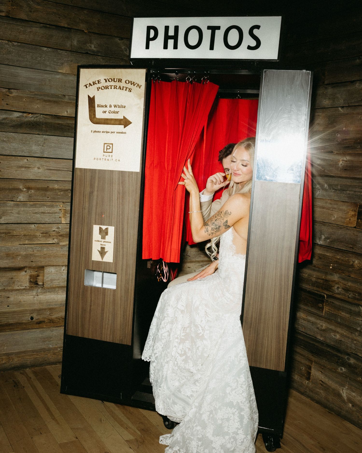 Bride in white lace gown posing inside a vintage photo booth with red curtains at a rustic wedding venue taken by Melissa Choi photography