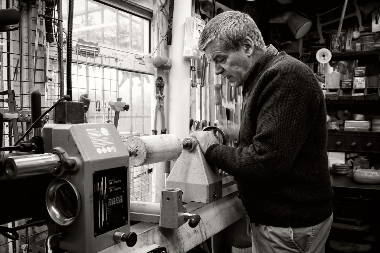 Black and white brand photograph of a wood turner working with a lathe in his workshop.