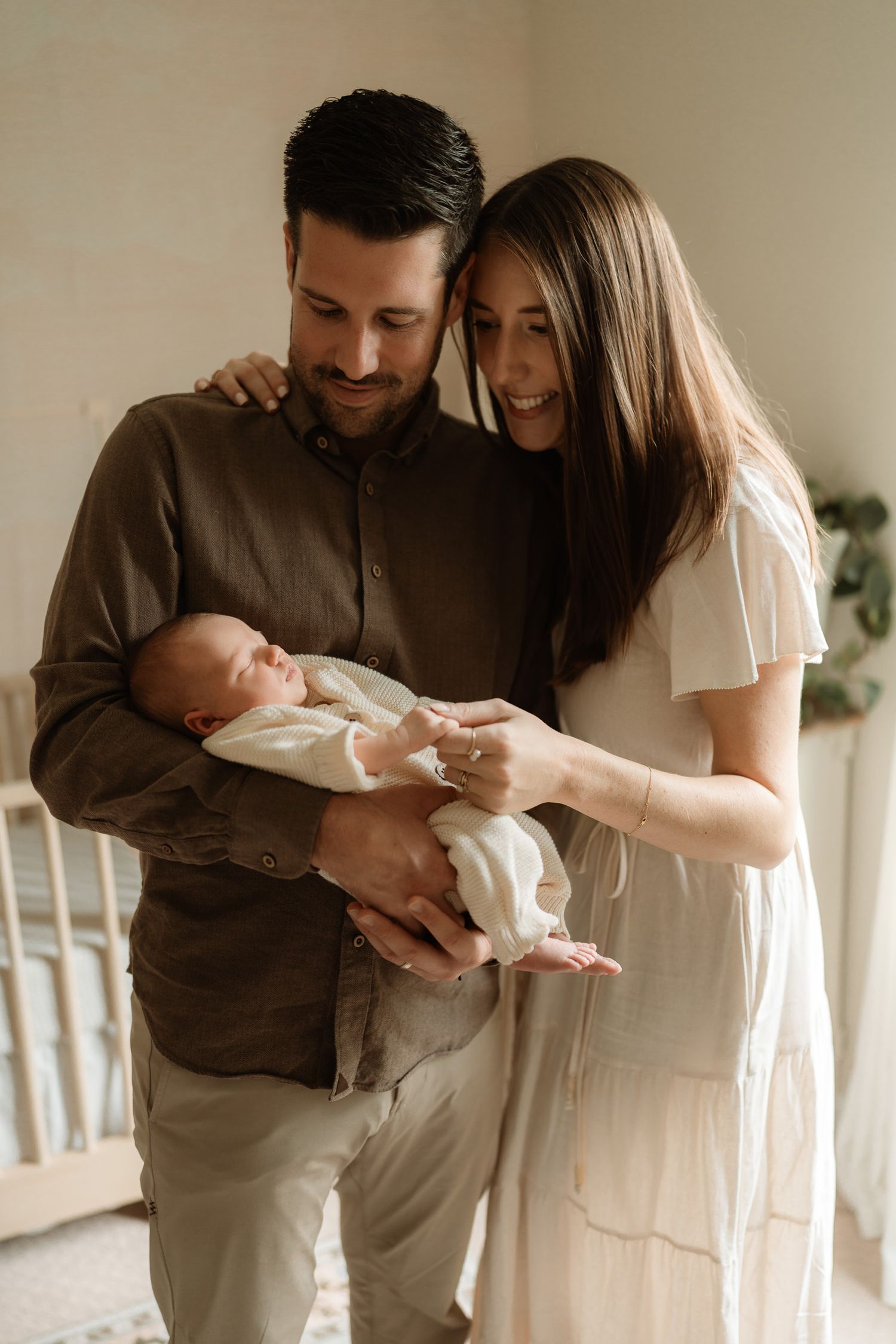 A couple smiles lovingly at their newborn baby, with the father cradling the infant in a warmly lit nursery.
