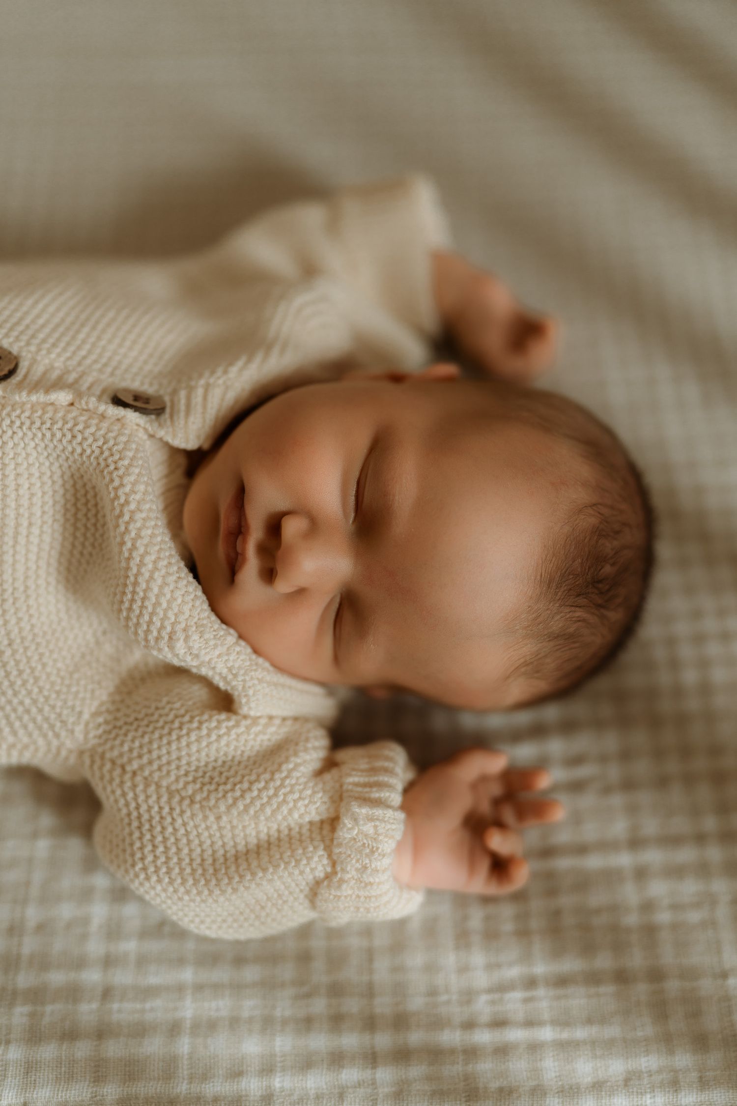 Sleeping newborn baby in cream knit onesie lying on soft checkered blanket.