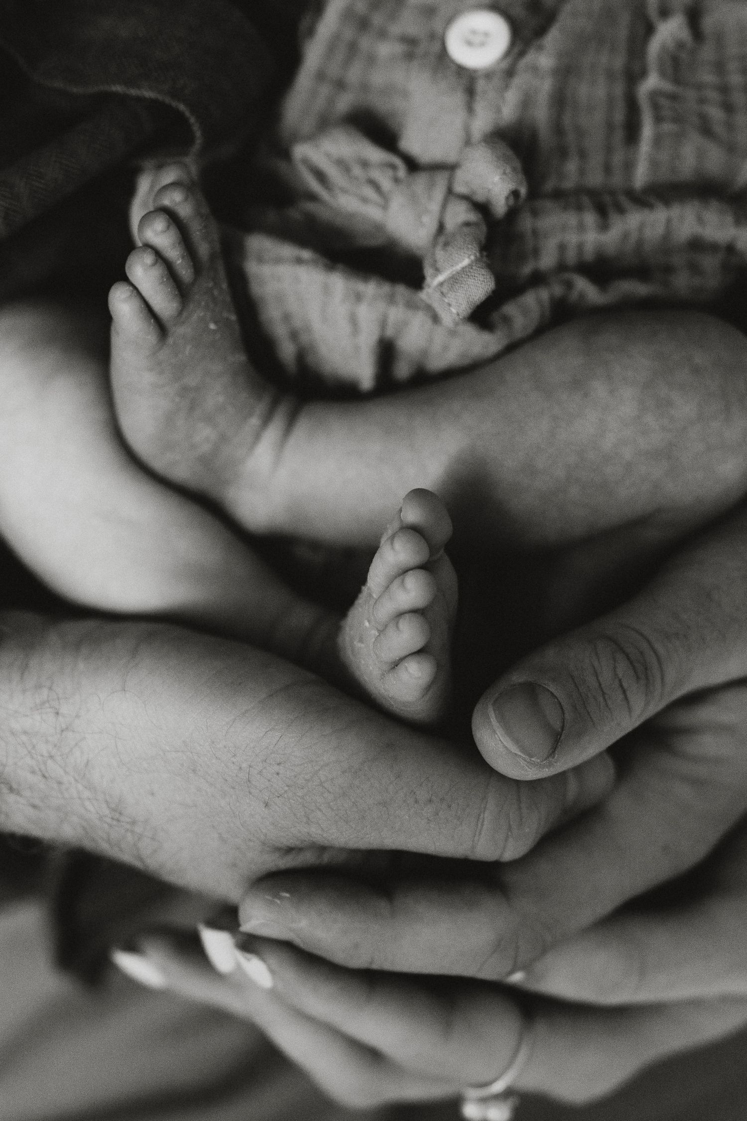 Black and white photo of tiny newborn baby feet cradled gently in adult hands, capturing a tender family moment.
