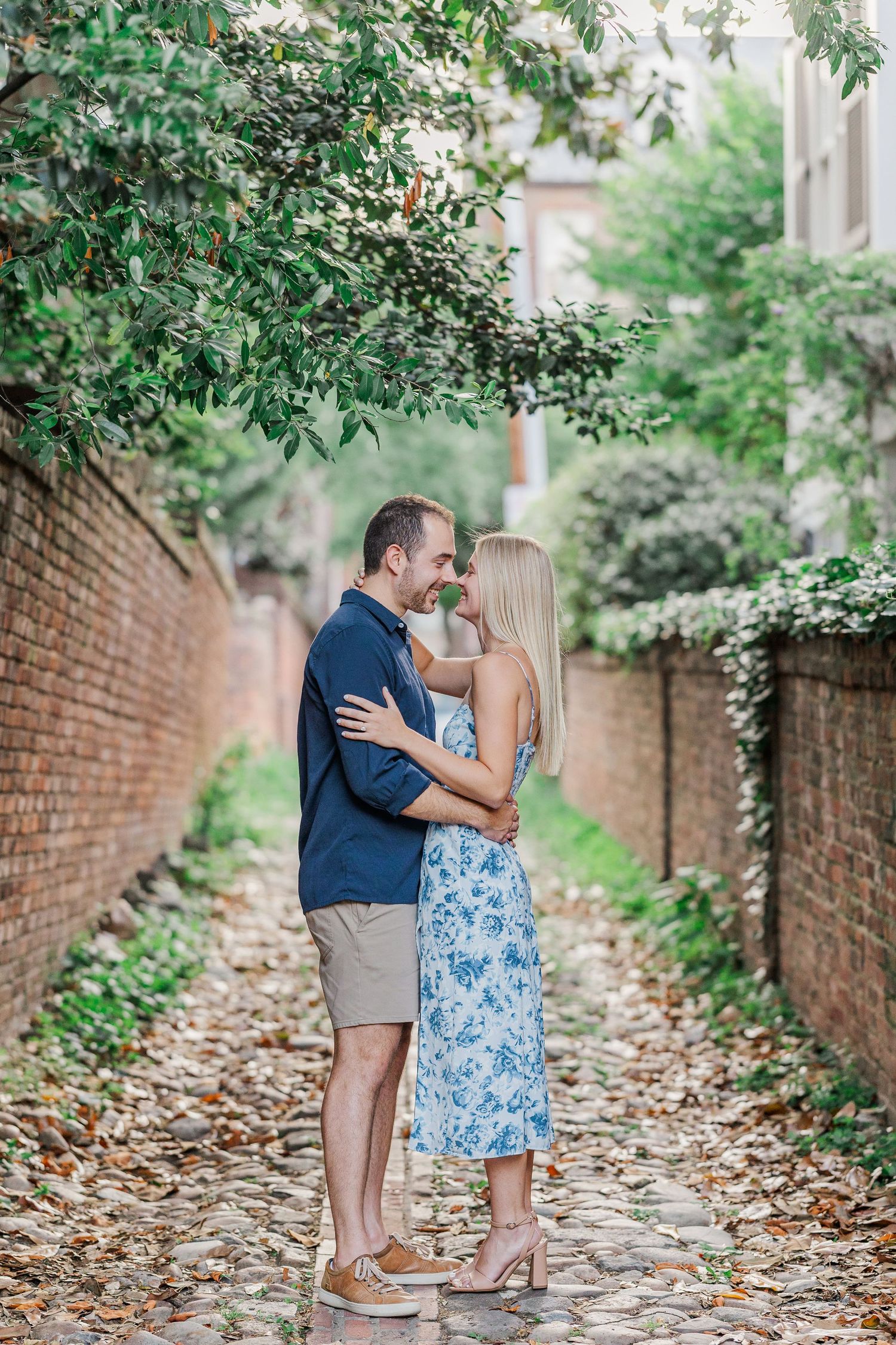 A couple embraces and smiles at each other in a lush garden, the woman in a blue floral dress holding the man's face.