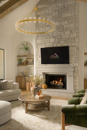 Elegant living room with stone fireplace, mounted TV, vaulted ceiling, gold chandelier, green velvet chair, and neutral decor.