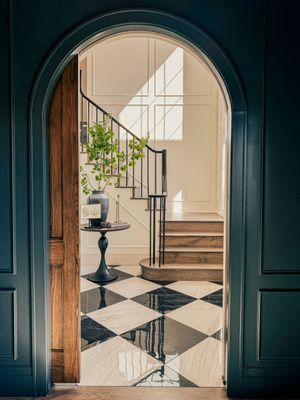 Elegant foyer with black and white checkered marble floors, arched doorway, curved staircase, and dark teal walls.
