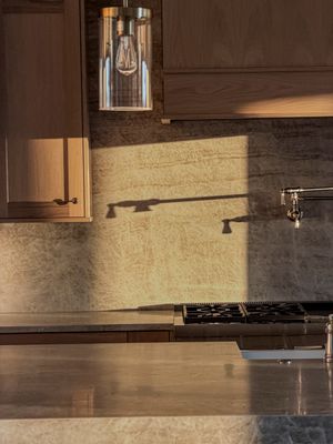 Warm kitchen backsplash with marble tile, wood cabinets, gas stove, and pendant light casting dramatic shadows in golden light.
