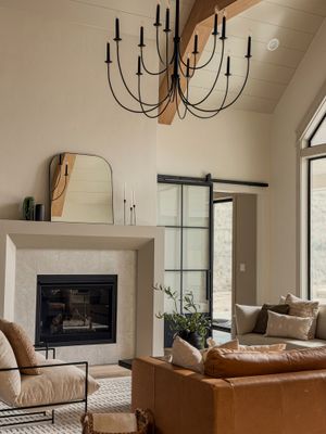 Modern living room with stone fireplace, leather sofa, black chandelier, and sliding glass barn door in neutral tones.
