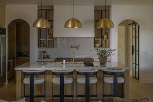 Modern kitchen with gold dome pendant lights, marble island, bar stools, and arched doorways.