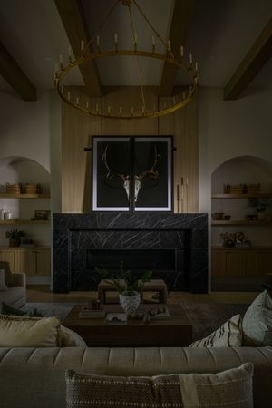 Dramatic living room with black marble fireplace, deer skull art, gold chandelier, and built-in shelving.