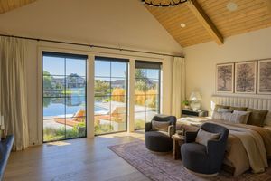 Bright master bedroom with vaulted wood ceiling, large sliding doors, pool view, and cozy seating area.