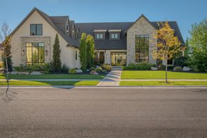 Elegant modern home exterior with stone and stucco facade, black-framed windows, and lush green lawn.
