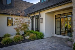 Modern home exterior with stone facade, black-framed windows, wall lanterns, and manicured landscaping on a patio.