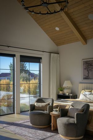 Vaulted wood ceiling bedroom with gray armchairs, sliding glass doors, and views of golden ornamental grasses.