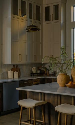 Modern kitchen with white upper cabinets, dark wood lower cabinets, gold hardware, marble island, and two upholstered bar stools.