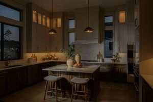 Modern kitchen with dark wood cabinets, pendant lights, white island, and bar stools in warm ambient lighting.