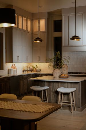 Modern kitchen with dark lower cabinets, pendant lights, white countertops, island with stools, and warm under-cabinet lighting.