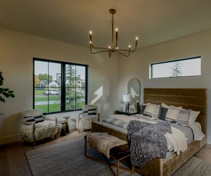 Elegant master bedroom with velvet headboard, chandelier, large windows, and neutral tones in a modern luxury home.