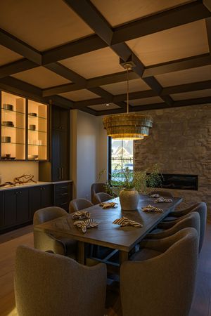 Elegant dining room with coffered ceiling, woven pendant light, stone fireplace wall, upholstered chairs, and dark wood table.