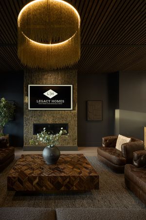 Luxurious dark living room with leather sofas, herringbone coffee table, stone fireplace, and dramatic fringe chandelier.