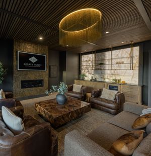 Luxury living room with leather sofas, wood ceiling, oval chandelier, stone fireplace, and elegant bar area.