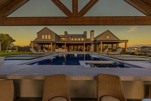 Luxury farmhouse estate with pool at sunset, viewed from covered outdoor bar with wicker seating.