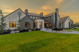 Luxury modern farmhouse exterior at sunset with stone accents, large windows, manicured lawn, and circular driveway.