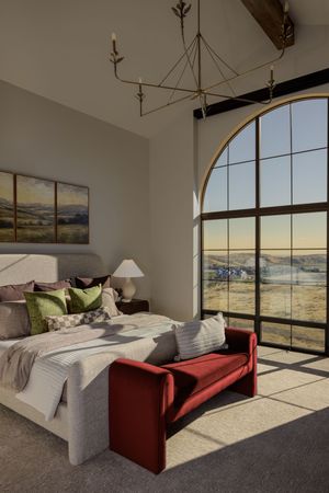 Elegant bedroom with arched window overlooking scenic landscape, red velvet bench, upholstered bed, and brass chandelier.