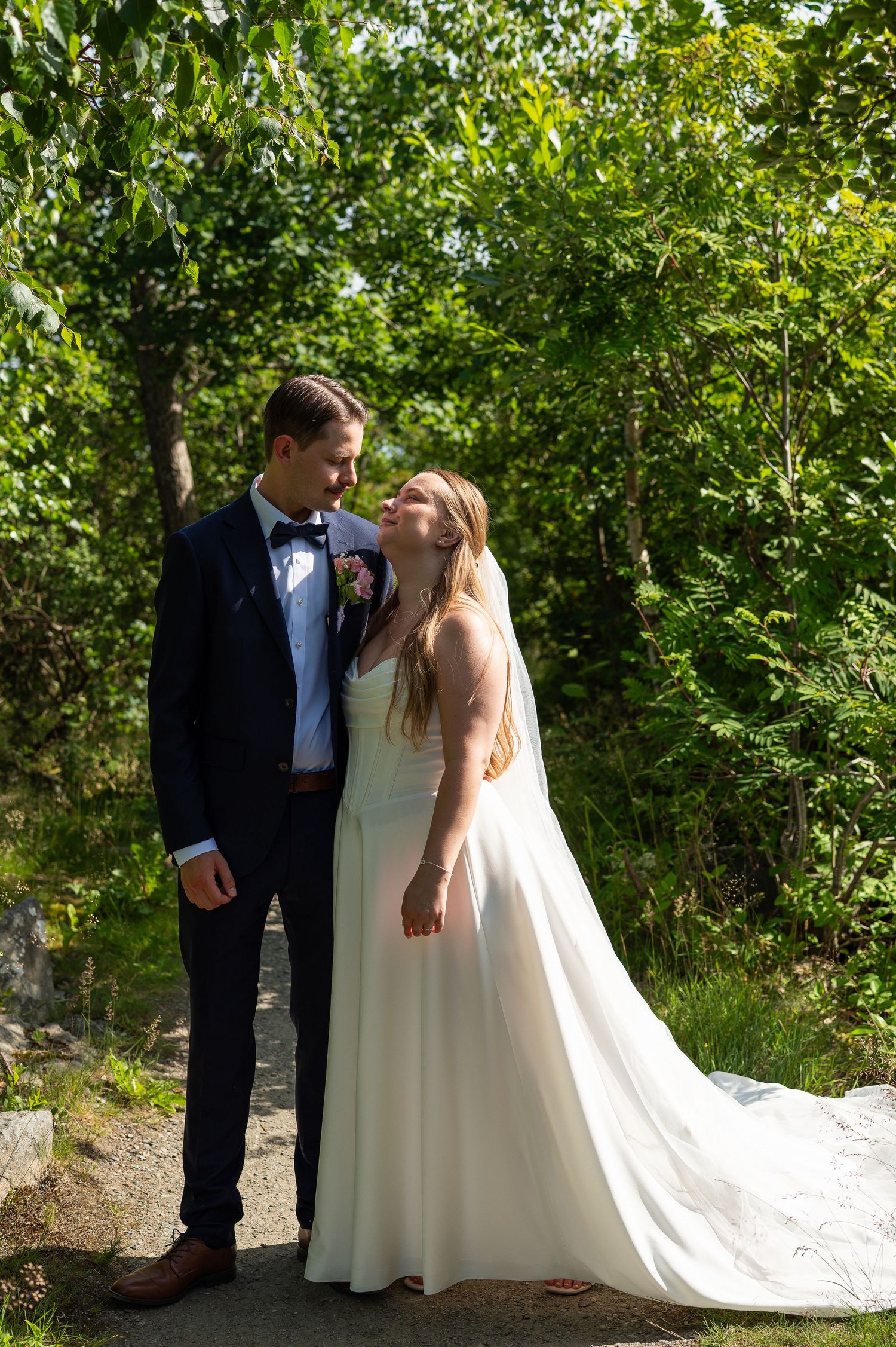 Bride and groom share a romantic moment outdoors, surrounded by lush green trees on their wedding day.