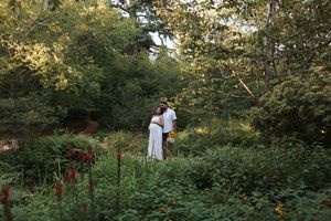 Couple embracing in a lush garden surrounded by colorful flowers and green trees during golden hour.