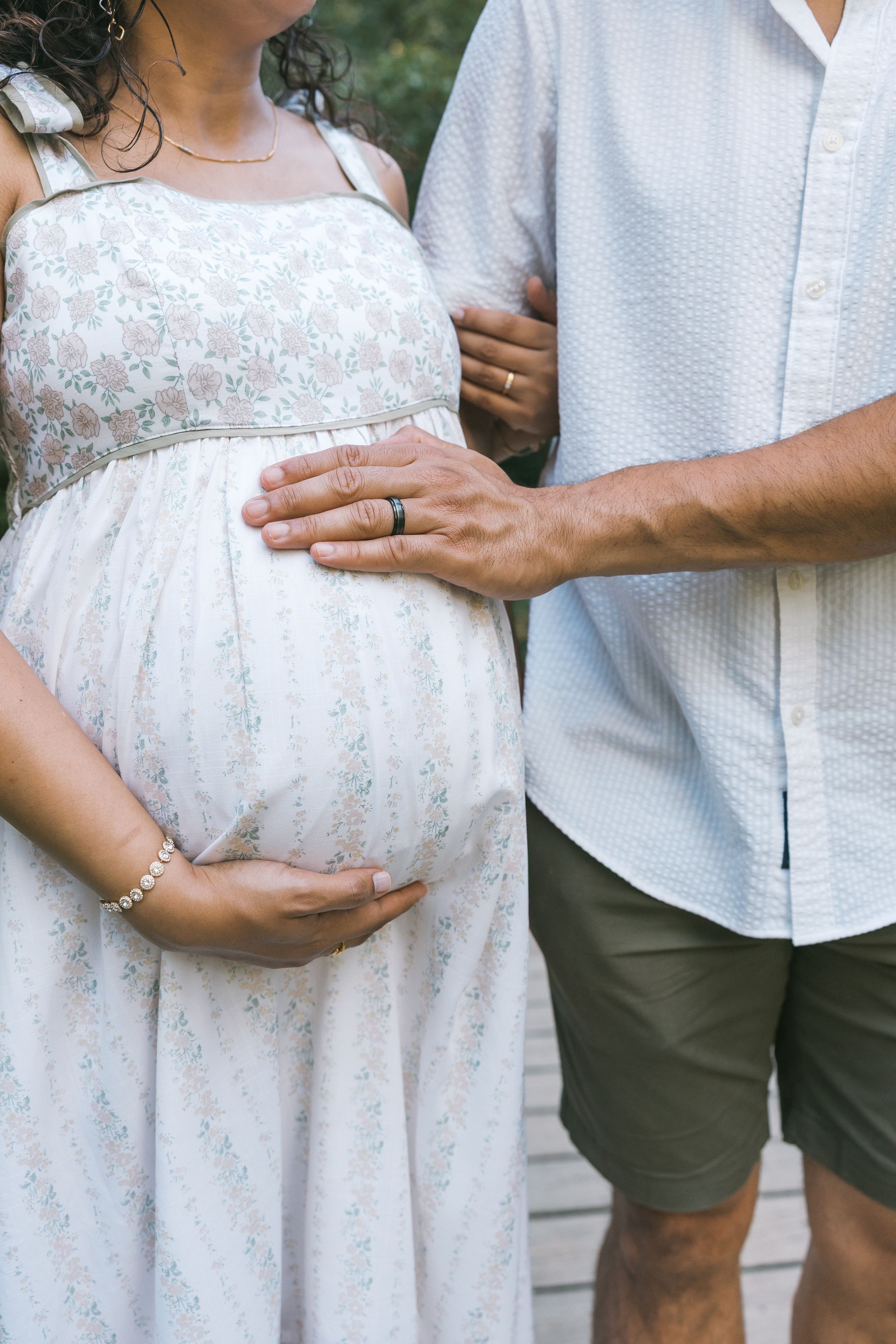 Couple expecting a baby, with man placing hand on pregnant womans belly outdoors.