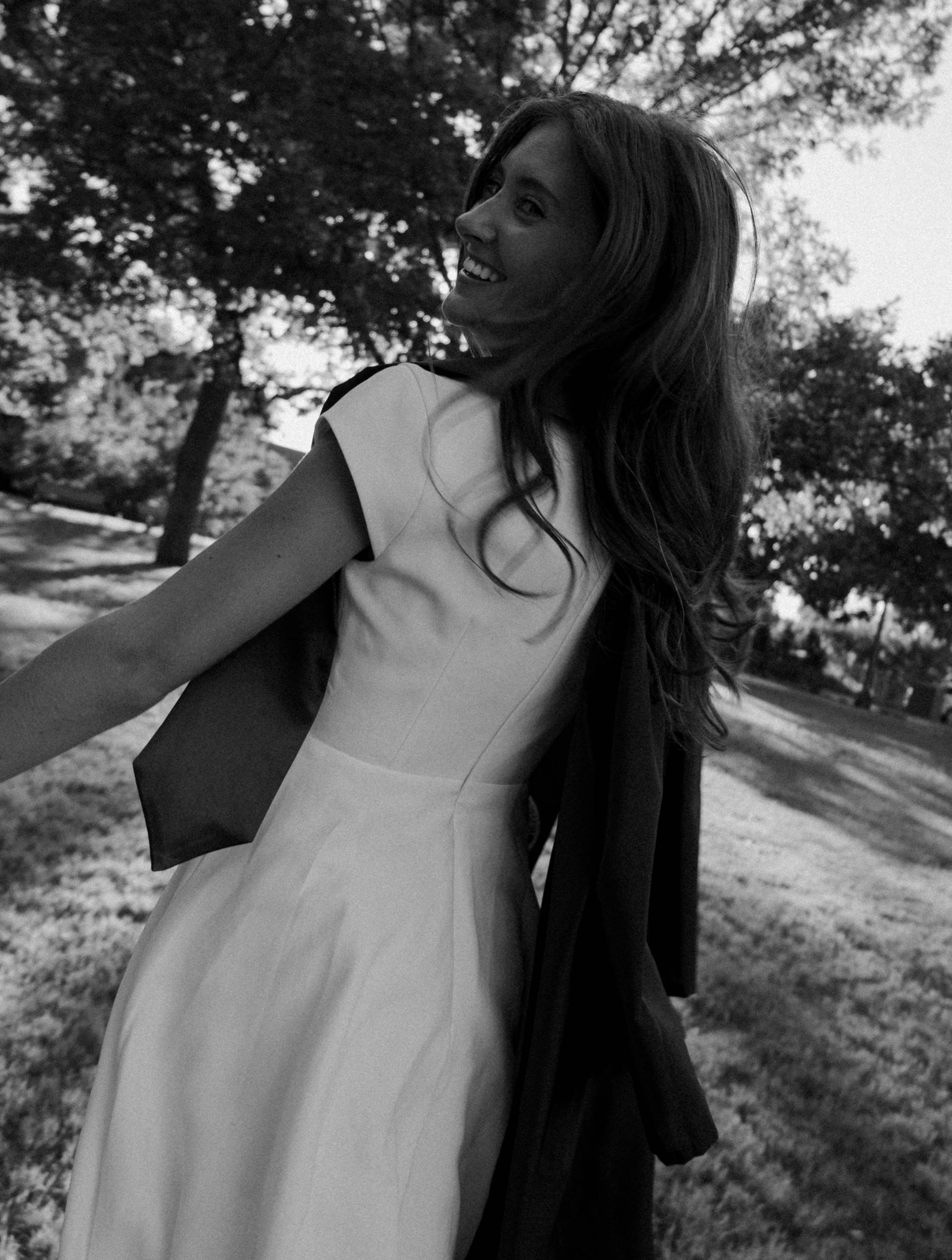 Black and white photo of a woman in a white dress twirling outdoors among trees.